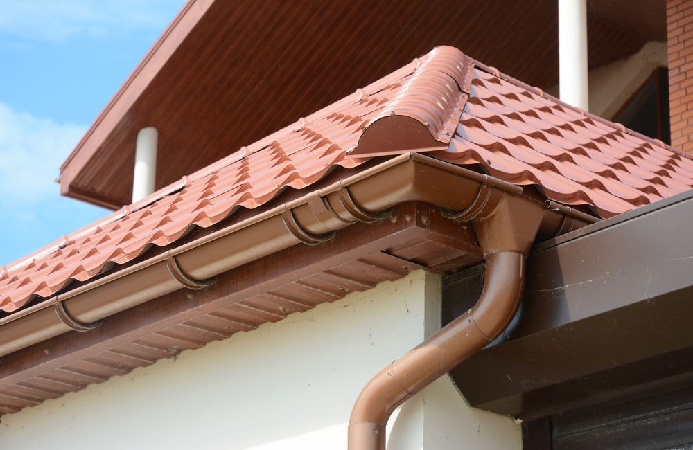 Close up on roof gutter holder and guttering downspout pipe with clay tiles roof. Installing rain gutter.