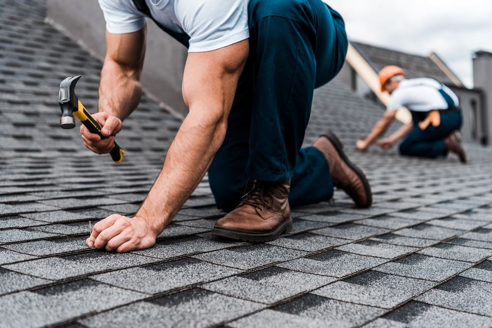 Man nailing a nail into shingles while repairing a roof